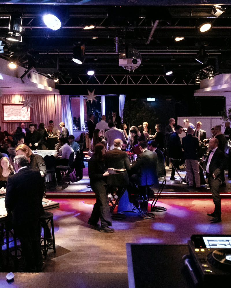 Gäste einer Firmenfeier an Spieltischen, der Saal in blaues und magentafarbenes Licht getaucht