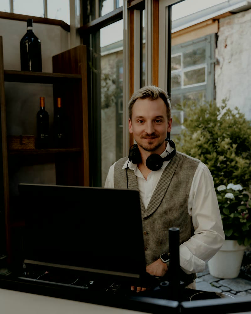 Andreas Stefani mit Kopfhörern um den Hals am DJ-Pult, im Hintergrund eine helle Fensterfront